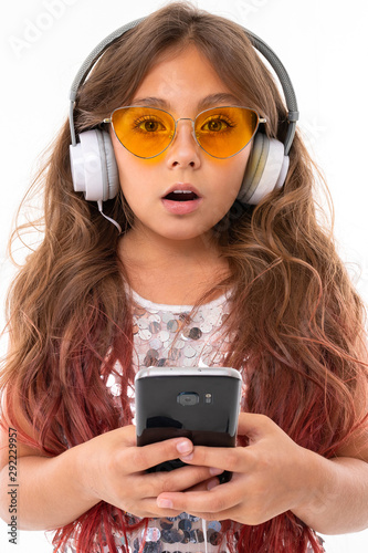 Surprised girl in yellow sunglasses, with big earphones holding black smartphone isolated © Ivan Traimak