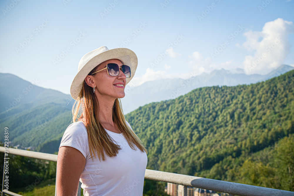 girl tourist in glasses white hat on the background of mountains looking forward