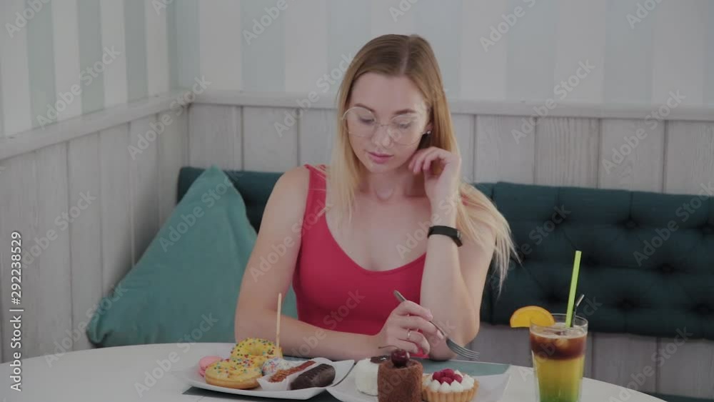 Beautiful young girl sitting at a table in a cafe with a plate of desserts. Beautiful young girl sitting at a table in a cafe with a plate of desserts.