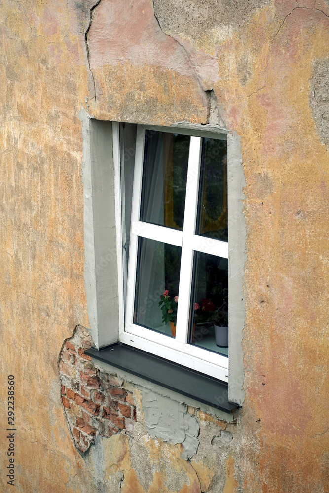 An opened new plastic window with white frame on threadbare house wall covered with plaster side view vertical closeup