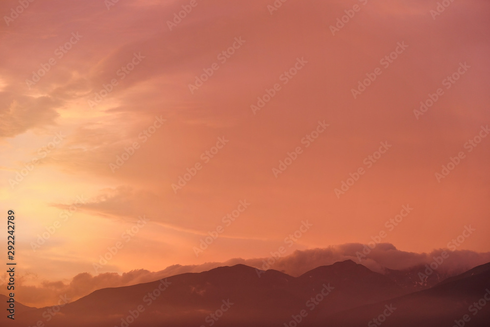 Orange and pink sky after sunset, silhouettes of mountains below - can be used as background with subjects placed in front
