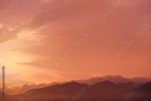 Orange and pink sky after sunset, silhouettes of mountains below - can be used as background with subjects placed in front