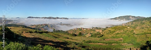 High resolution panorama - typical Madagascar landscape at Alakamisy Ambohimaha region fog rolls over green valley with terraced rice field, clay houses on small hills, higher mountains in background