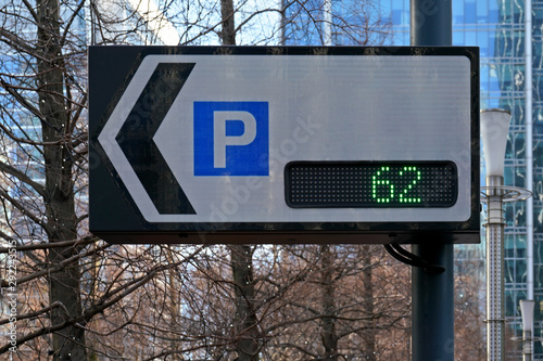 Traffic sign board showing number of parking spaces and arrow pointing to park lot, text can be added to white space, blurred trees and buildings background