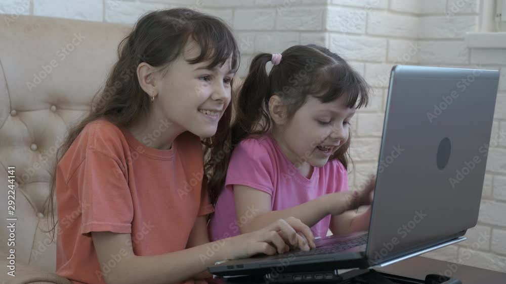Children play on notebook. Happy little sisters play computer games together. Children play on notebook. Happy little sisters play computer games together.