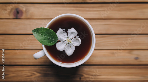 White cup of tea with petals of an apple tree on a wooden background  view from above  close up.