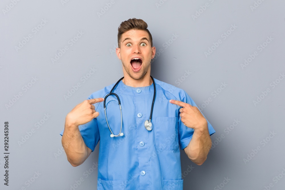 Young nurse man surprised pointing at himself, smiling broadly. Young nurse man surprised pointing at himself, smiling broadly.