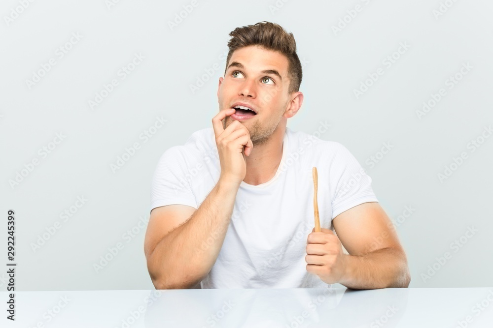 Young man holding a toothbrush relaxed thinking about something looking at a copy space. Young man holding a toothbrush relaxed thinking about something looking at a copy space.