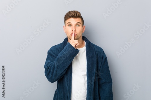 Young caucasian man wearing pajama keeping a secret or asking for silence.