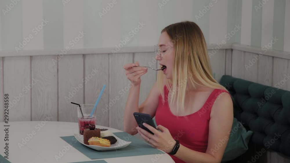 A beautiful young girl uses a mobile phone in a restaurant at a table, around her is a plate with desserts. A beautiful young girl uses a mobile phone in a restaurant at a table, around her is a plate with desserts.