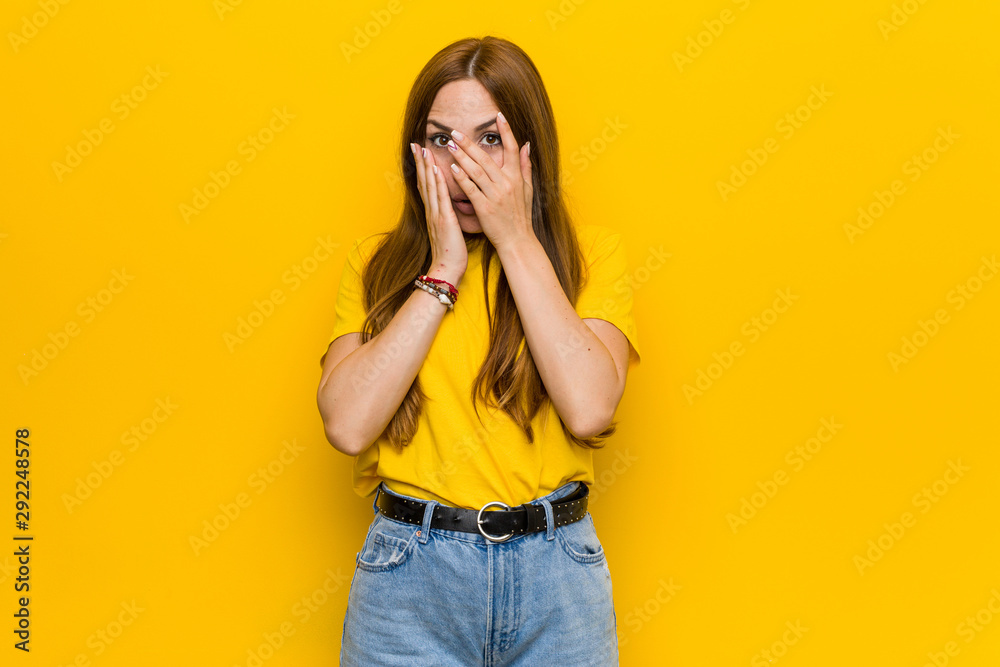 Young ginger redhead woman blink through fingers frightened and nervous.