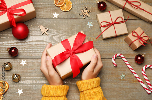 Young woman holding Christmas gift on wooden background, flat lay