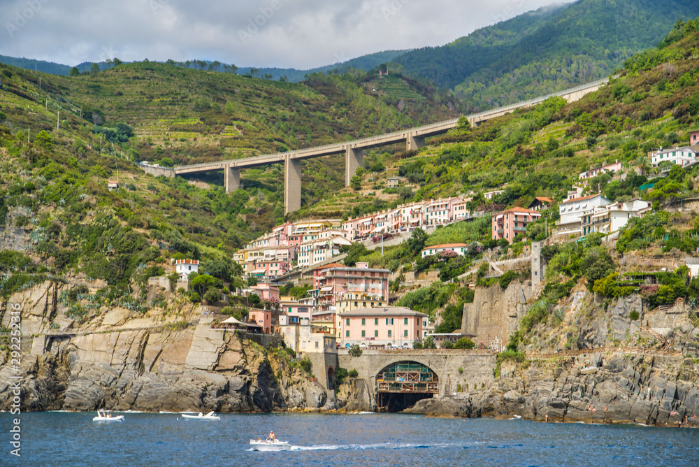 Riomaggiore, Cinque Terre, Italy - August 17, 2019: Village by the sea bay, colorful houses on the rocky coast. Mountains in the vegetation. The bridge in the mountains.