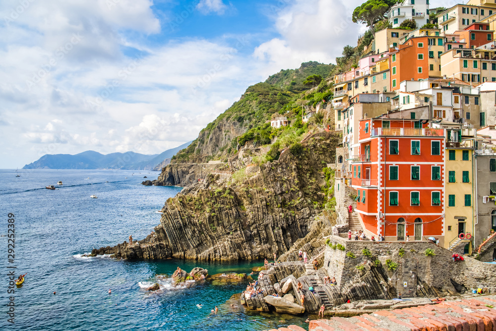 Riomaggiore, Cinque Terre, Italy - August 17, 2019: Village by the sea bay, colorful houses on the rocky coast. Nature reserve resort popular in Europe. Small beach