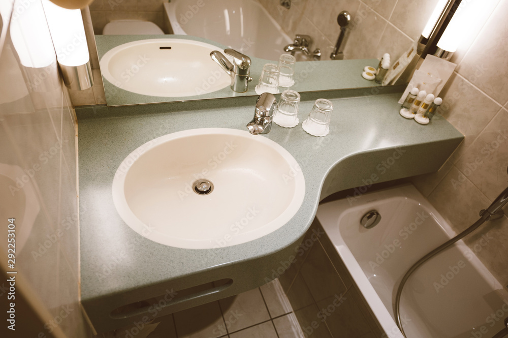 Interior of modern three star hotel bathroom with sink, chrome water tap , two glasses and defocused shampoo in the corner Interior of modern three star hotel bathroom with sink, chrome water tap , two glasses and defocused shampoo in the corner