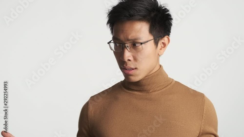 Young stylish perplexed asian man in eyeglasses over white background. What is going on expression