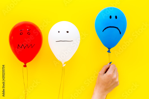 Negative emotions concept. Balloons with drawn faces on yellow background top view