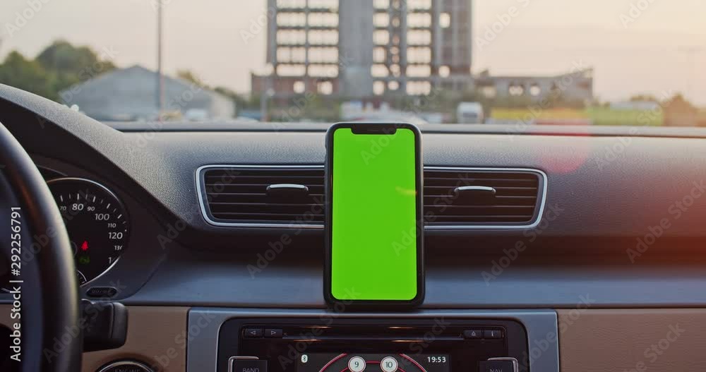 Young man using mobile navigation app on mounted mock-up vertical smartphone greenscreen inside modern car. Sunset. Close-up. Young man using mobile navigation app on mounted mock-up vertical smartphone greenscreen inside modern car. Sunset. Close-up.