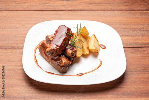 Barbecue pork ribs with potato wedges isolated in white plate on wooden background