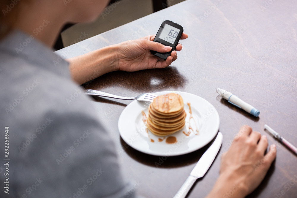 selective focus of woman with diabetes holding glucose monitor near pancakes