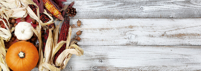 Autumn holiday concept with corn, gourd, pumpkin and acorns on white wood background in overhead view