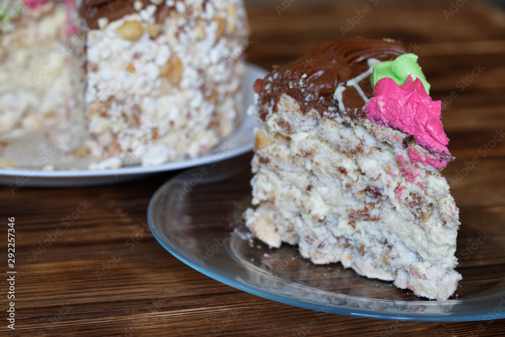 A piece of sponge cake with meringue, peanuts and cream flowers lies in a transparent plate on a wooden background. Macro A piece of sponge cake with meringue, peanuts and cream flowers lies in a transparent plate on a wooden background. Macro