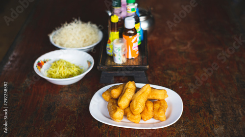 Asian congee with minced pork, sliced ginger, vegetable and mini deep-fried dough sticks in glass bowl on wooden table. a delicious traditional Asian food style