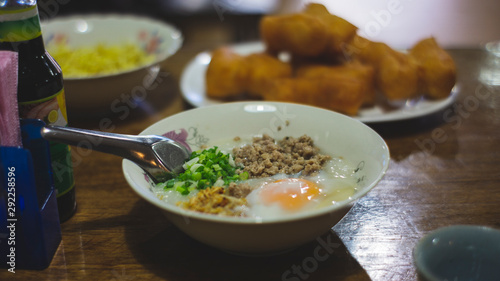 Asian congee with minced pork, sliced ginger, vegetable and mini deep-fried dough sticks in glass bowl on wooden table. a delicious traditional Asian food style
