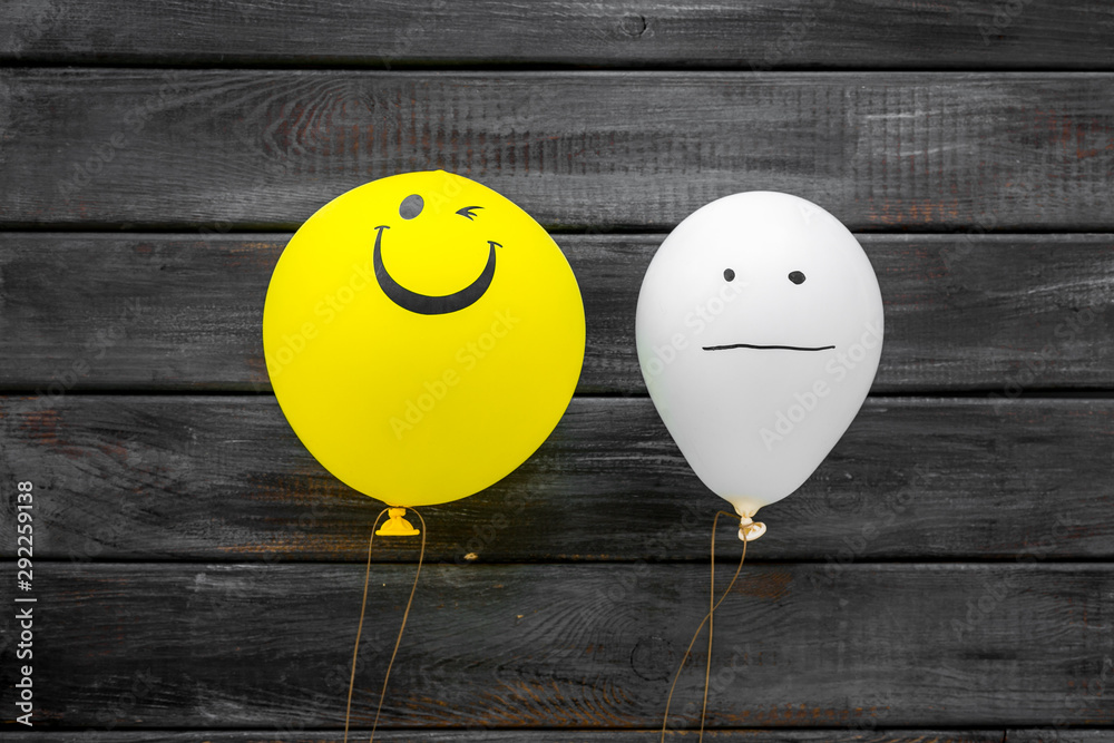 Naklejka Treat depression concept. Balloons with frustrated and smiling faces on dark wooden background top view