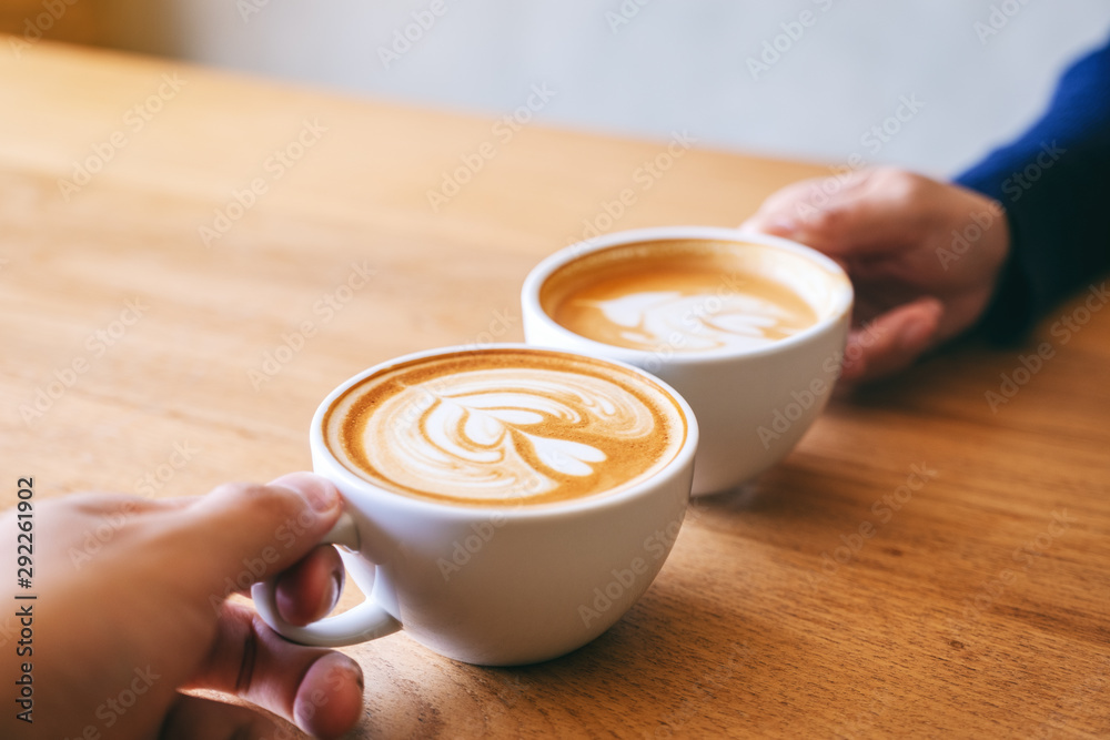 Fototapeta Close up image of a man and a woman clinking two coffee mugs on wooden table in cafe