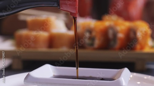female hands pour soy sauce from a mini-kettle into a pan, next to sushi