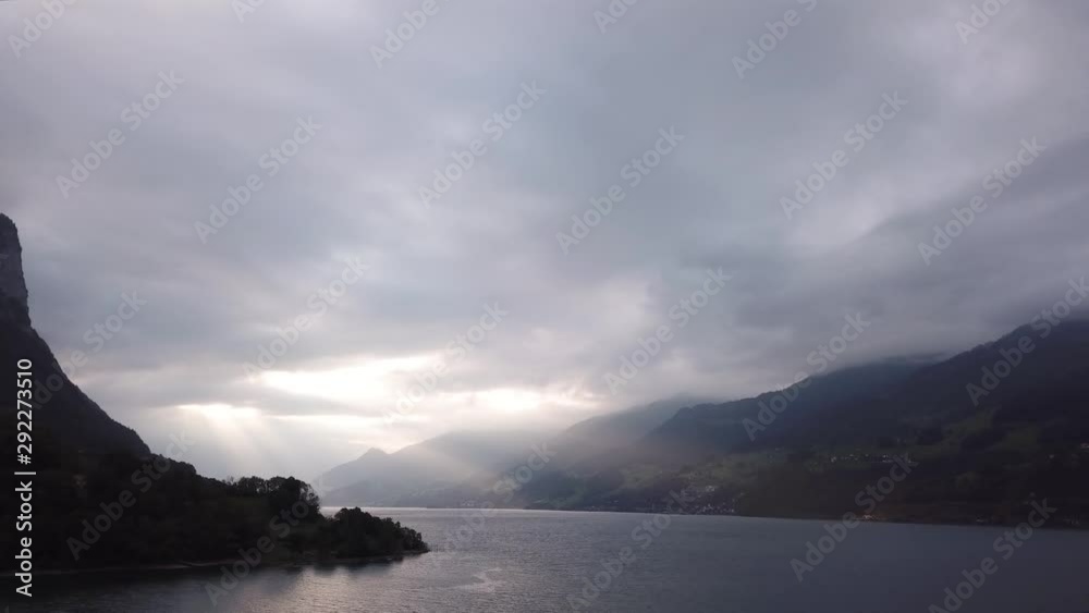 Flying over a large lake on a cloudy day with sun rays peeking through the clouds onto the mountains below. Flying over a large lake on a cloudy day with sun rays peeking through the clouds onto the mountains below.