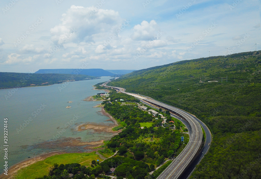 Fototapeta premium Picturesque asphalt road is meandering landscape with forests and mountains, The expressway that curves down the mountain and river with clouds and blue sky background. Local transportation concept.
