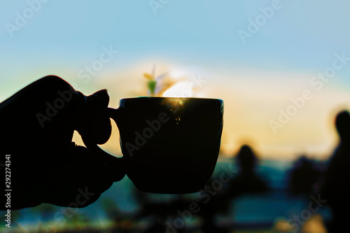 silhouette of hand holding with cup of coffee at sunset