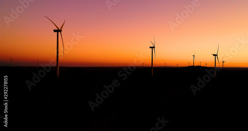Wind turbines under the orange sunset. This is a wind farm which produce sustainable energy, perfect for the environment - aerial view with a drone - environmental & ecological concept