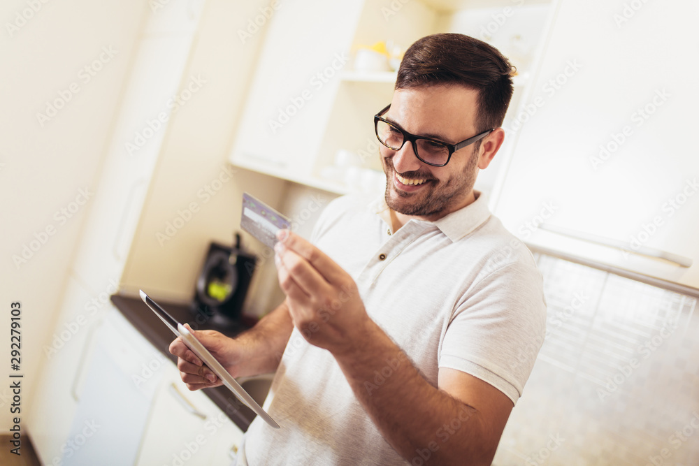 Happy man using digital tablet and credit card in kitchen at home