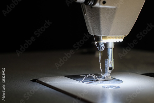 Close-up needle of white industrial sewing machine use sew cloth with black background.