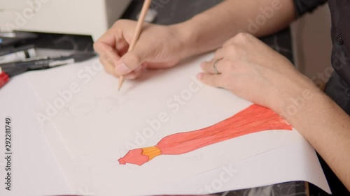 Static closeuup shot of a fashion designer painting a sketch of a dress at his desk. photo