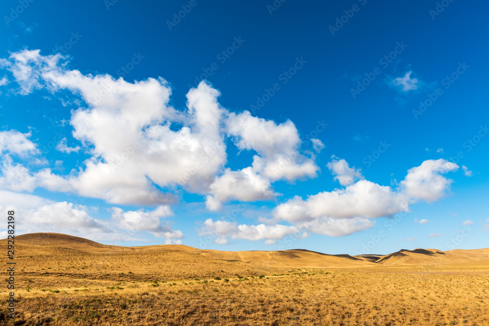 Clouds on a blue sky over mountains with dried yellow grass