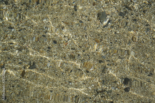 Coastal sand under water. Optics and distortion of light passing through water. Waves and sun flare. Pebbles. © Anatoliy
