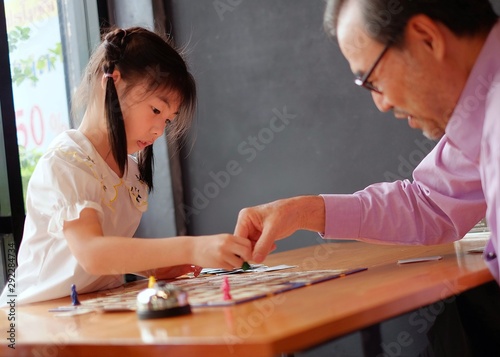An pretty Asian preschool girl learning to play board games with her grandfather