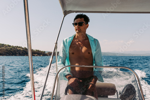 Man in sunglasses driving and navigating yacht in the sea. Sailing man on yacht in ocean