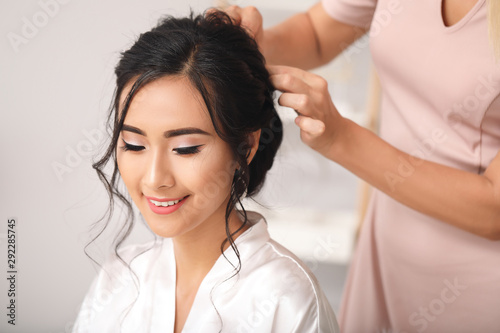 Professional hairdresser working with young Asian bride at home