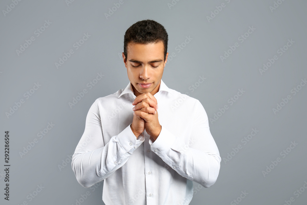 Young African-American man praying on grey background Young African-American man praying on grey background