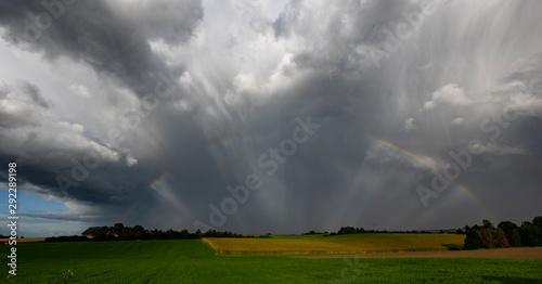 rainbow over a green and yellow field with grey clouds dramatic