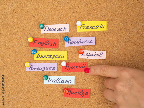 Woman's hand point to cards with different language names on a cork desk. Study foreign language concept photo