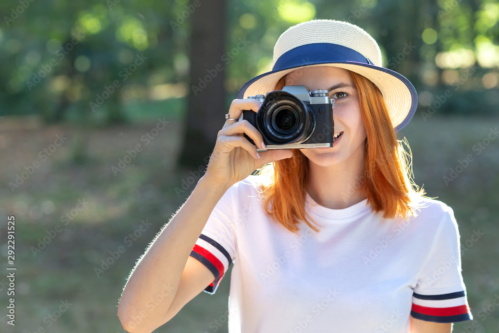 Pretty teenage girl with red hair taking picture with photo camera in summer park. Pretty teenage girl with red hair taking picture with photo camera in summer park.