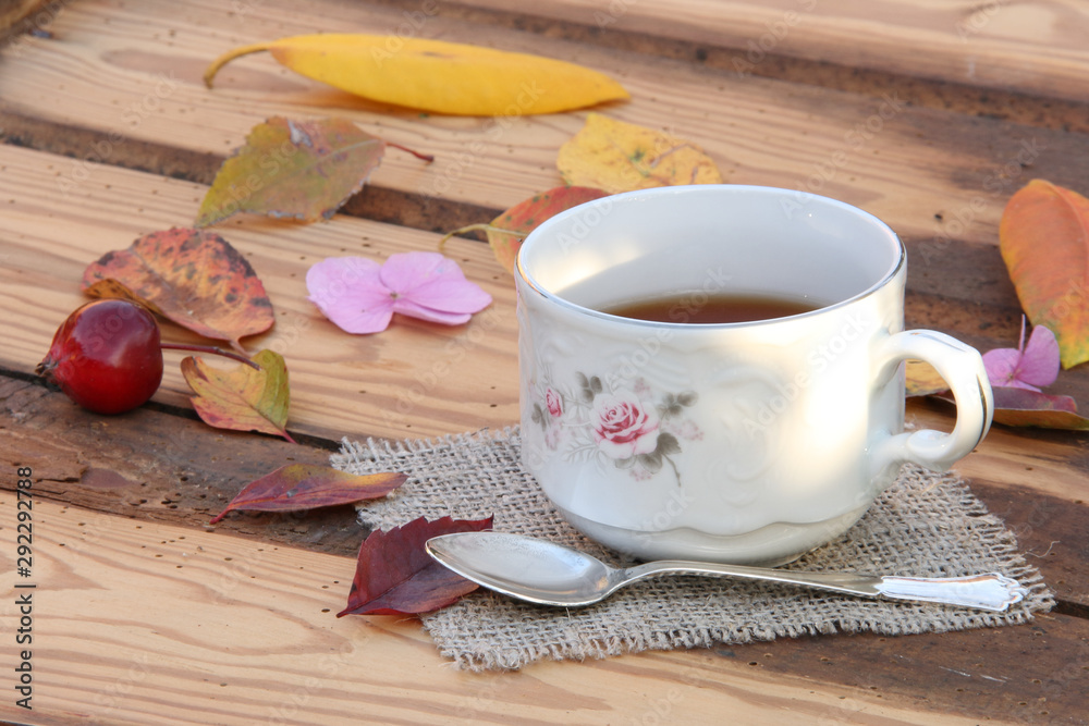 Cup with tea on a background of an old wooden table and autumn leaves of different colors Cup with tea on a background of an old wooden table and autumn leaves of different colors