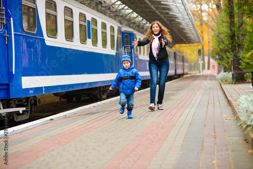 Mom catches up with laughing runaway little son along blue train at station