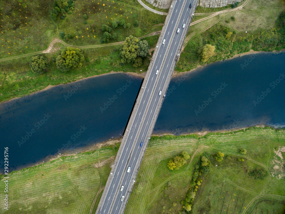 Landscape of an asphalt road with cars. View from above on the bridge and the blue river. Summer photography with bird's eye view.